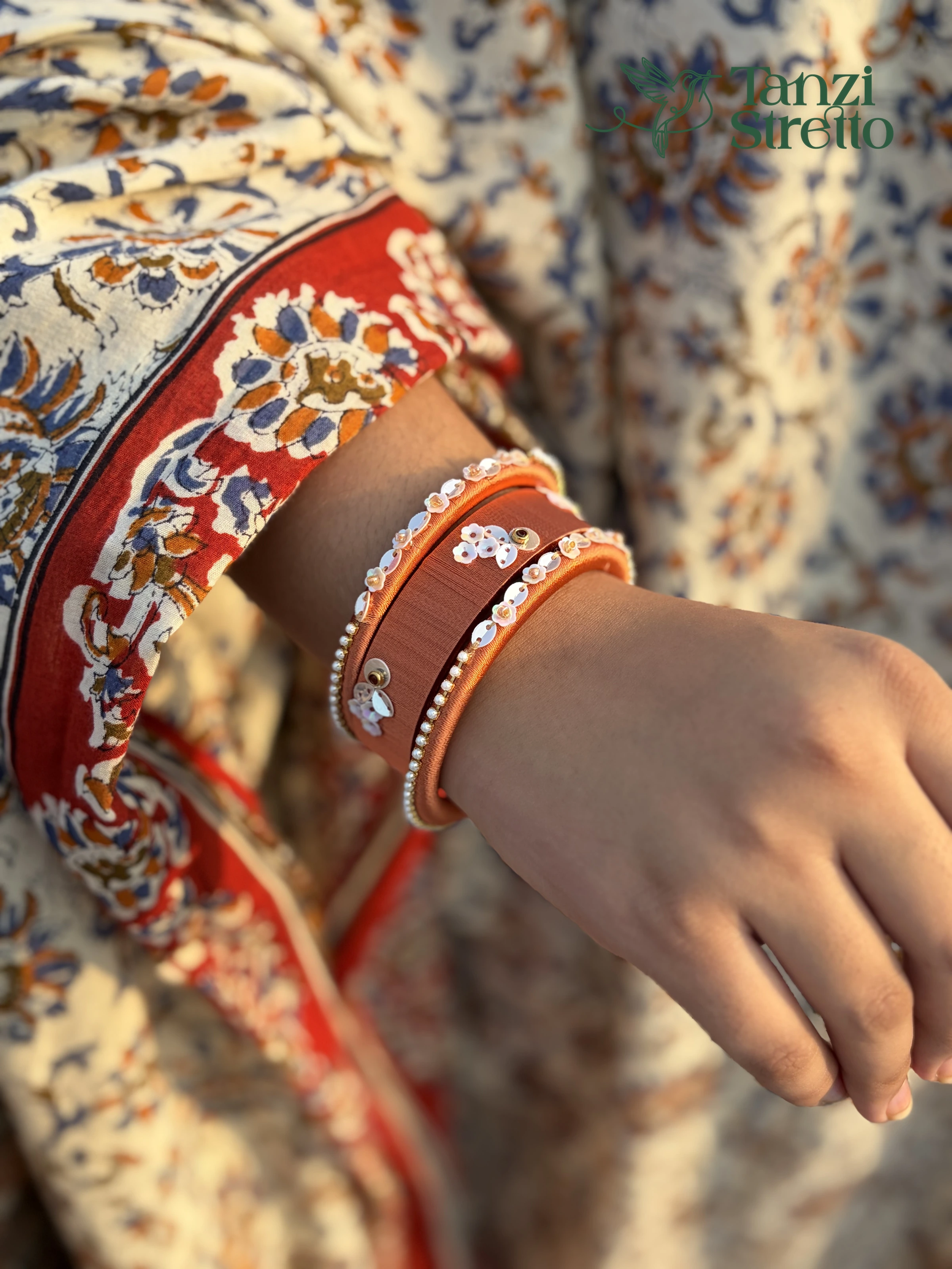 Rukmini burnt orange silk thread bangles with white flower sequins and pearl edges on a wrist