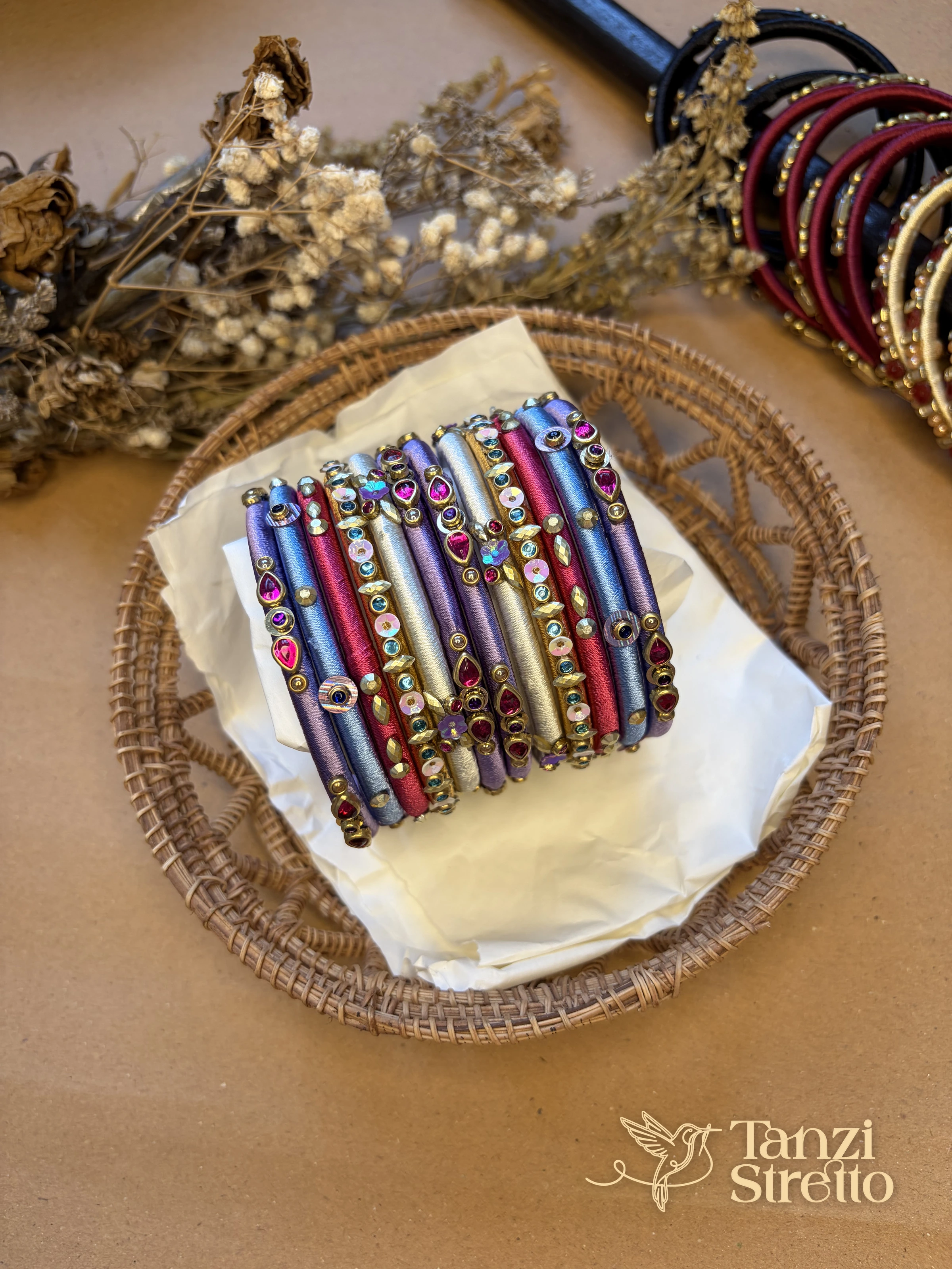 Anonya silk thread bangles in lavender, blue and pink with magenta teardrop stones, in a woven basket