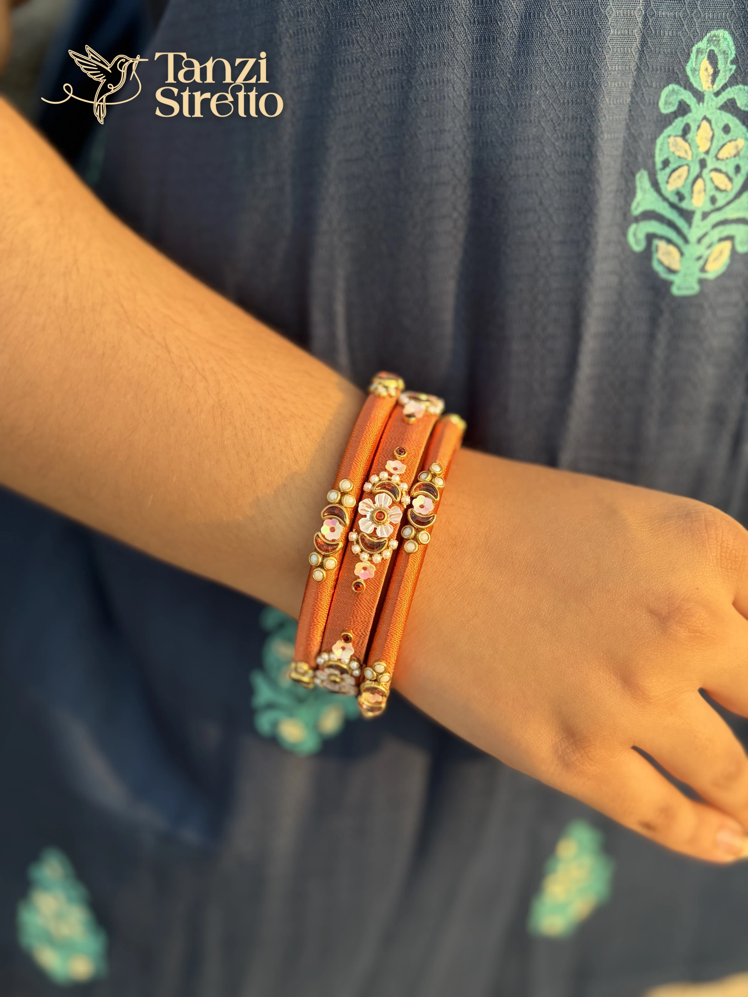 Shiuli saffron silk thread bangles with a white flower and crescent stones on a wrist