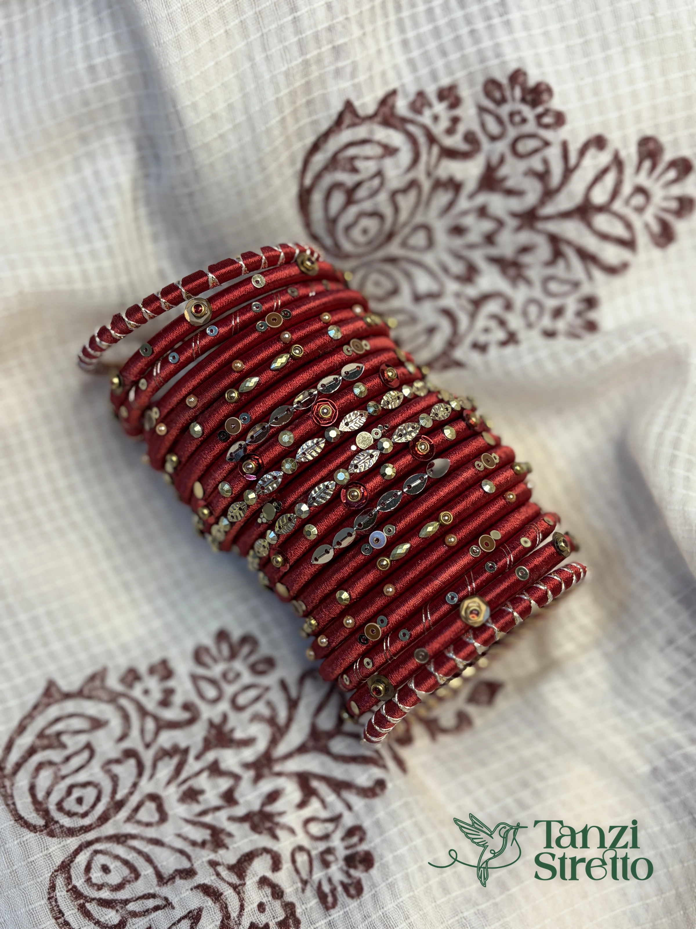 Obhishar red silk thread bangle stack on a white block-printed fabric